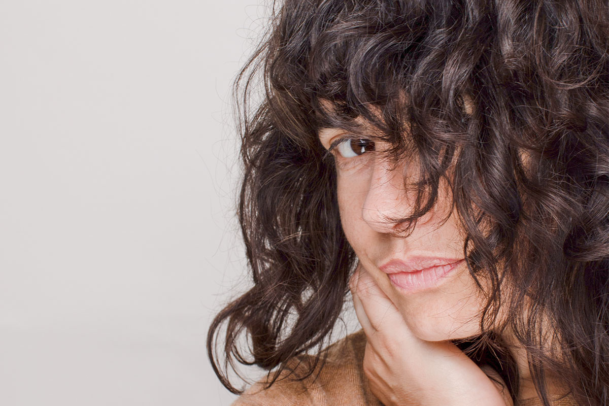 Closeup of a woman's face, half-covered with wavy hair. She is looking into the camera. 