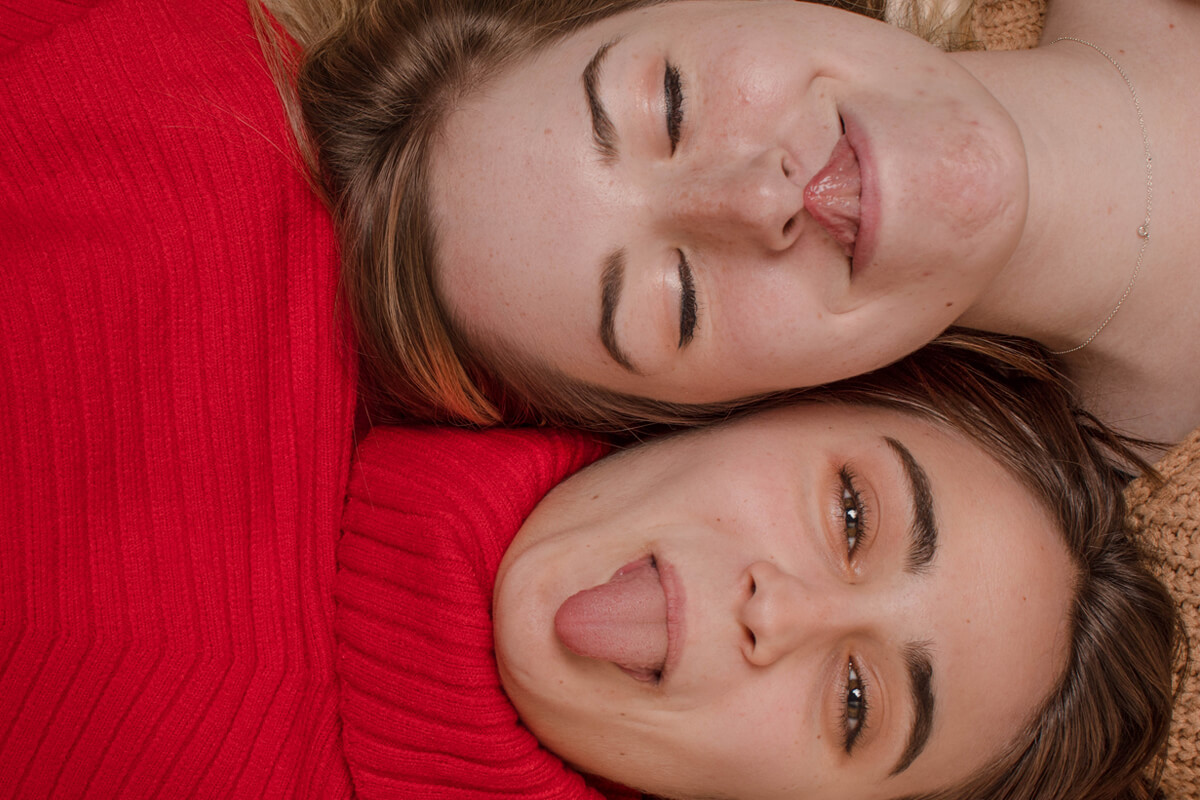 Two people laying cheek to cheek with their tongues out