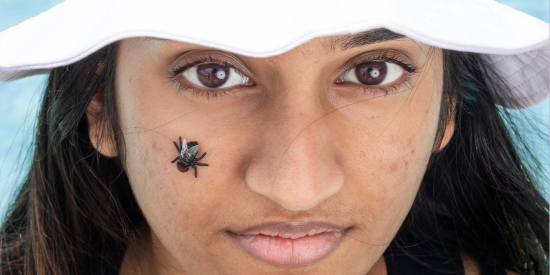 Close-up of a woman wearing a bucket hat with a fake bug on her cheek