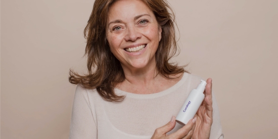 A woman smiling and looking into the camera while holding a bottle of Curology cream