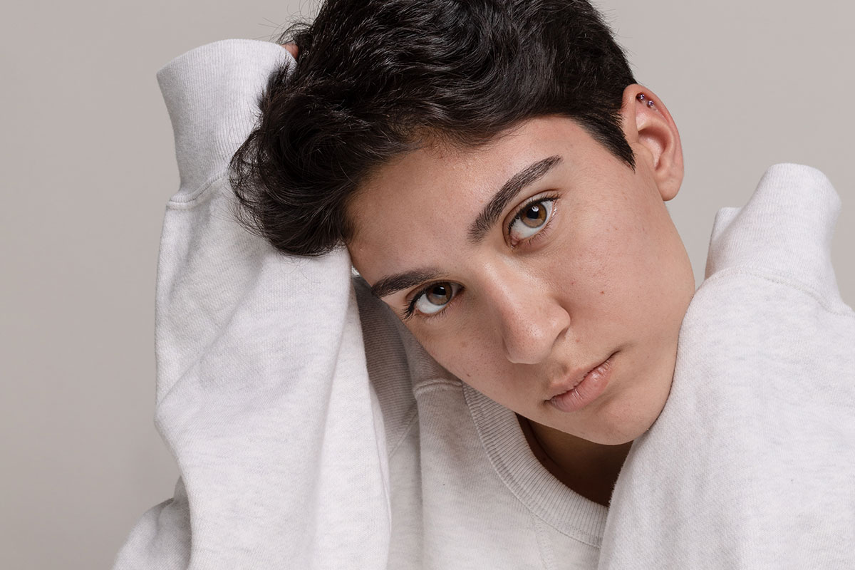 Person in white sweatshirt with head tilted in front of light neutral background