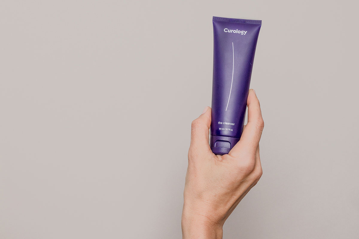 Hand holding Curology cleanser against a neutral background