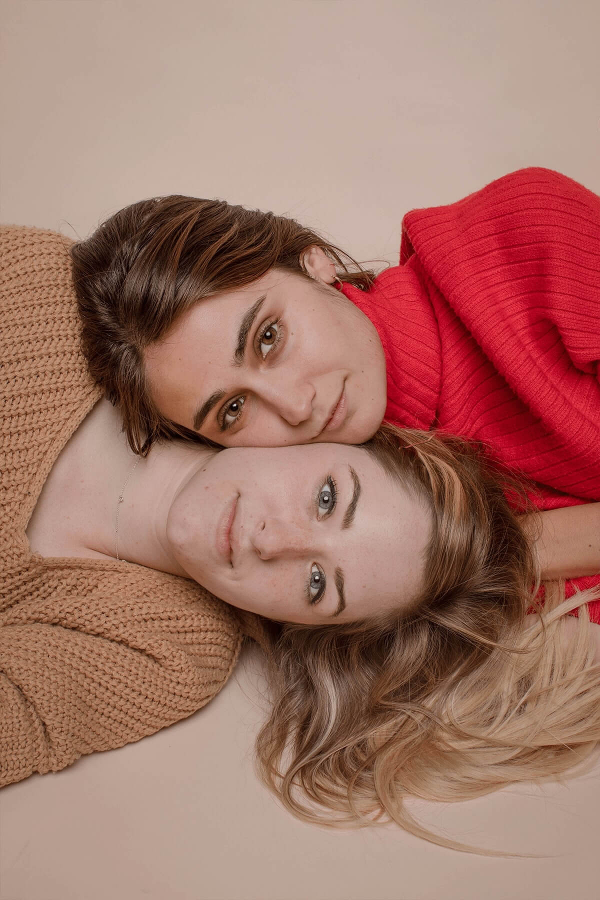 Women with faces / cheeks touching against a tan background