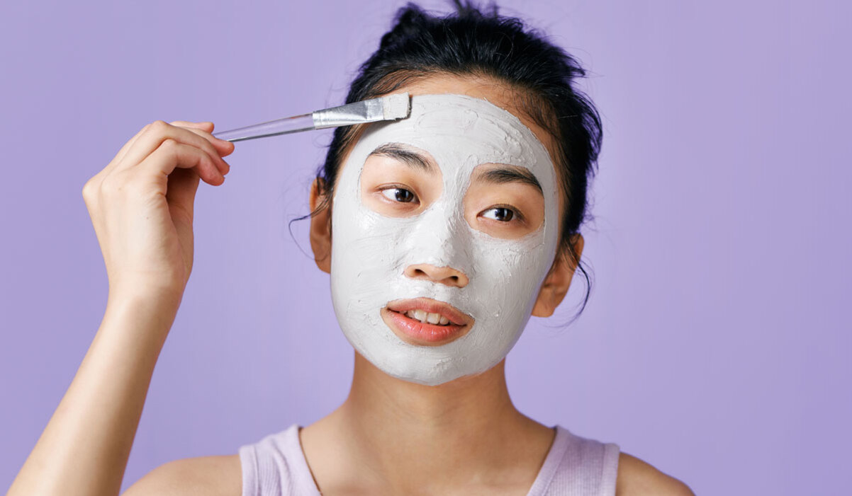 Woman applying exfoliating face mask to skin with brush