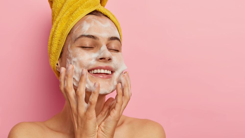 Young happy female washes face against pink background - The benefits of using beta-hydroxy acid in your skincare routine