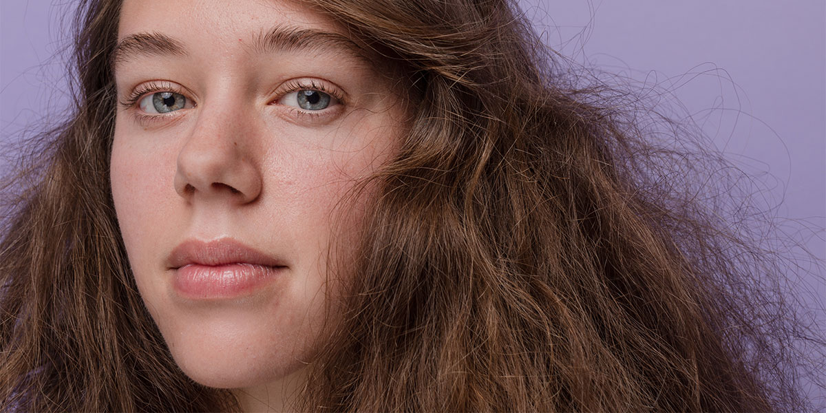 Woman with voluminous brown hair in front of purple background