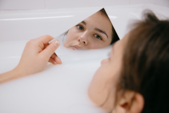 Woman on a bathtub looking at her face on a little mirror