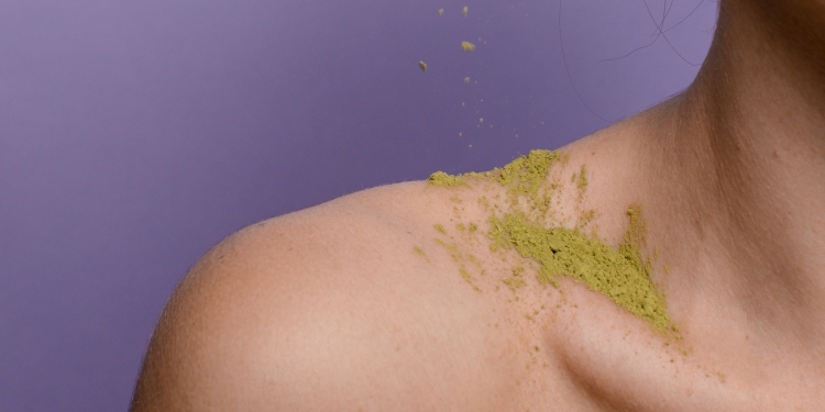 Closeup of collarbone and shoulder with green powder against a purple background