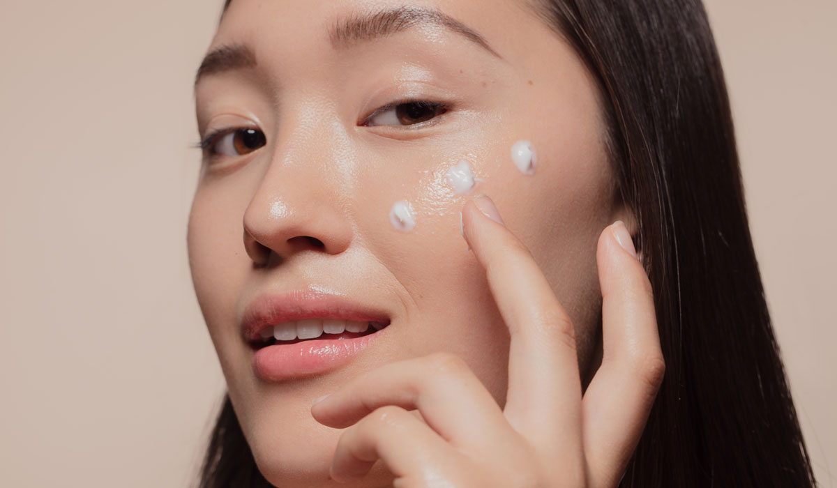 Asian woman applying skincare cream to face