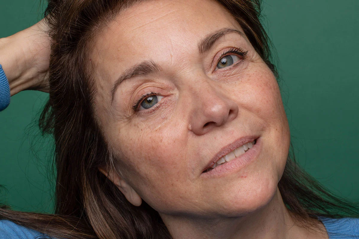 Woman with brown hair pulling hair away from forehead against a green background