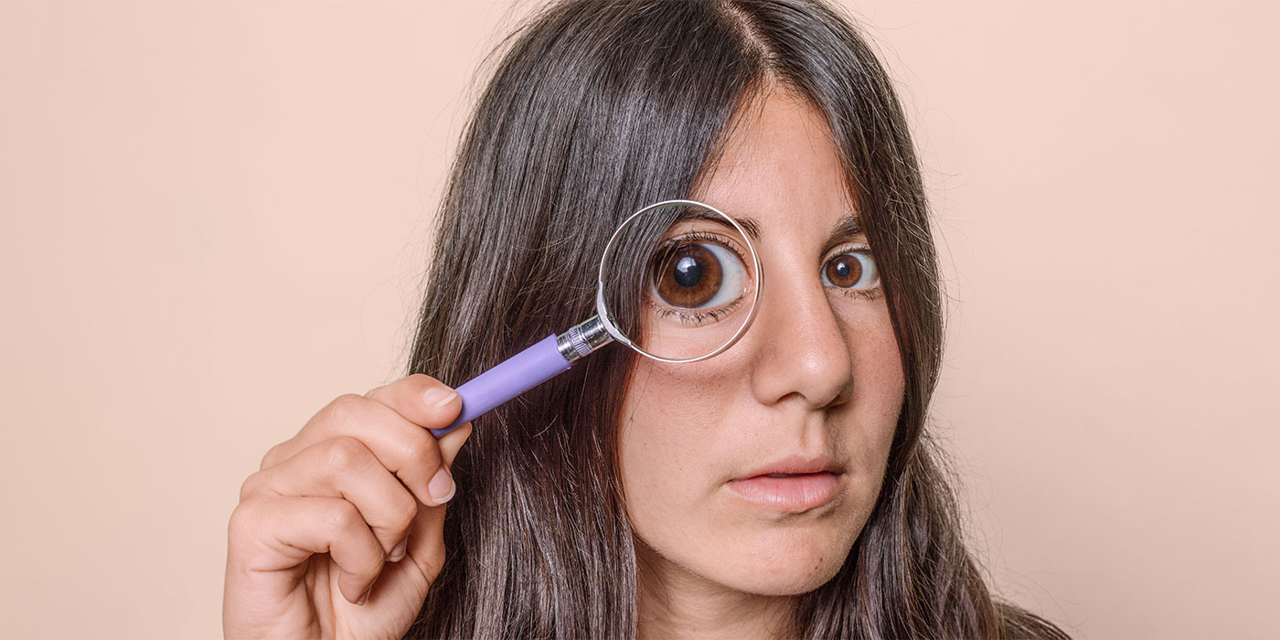 A woman holds a magnifying glass over one eye, making it appear larger. 