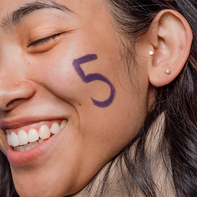 Closeup of woman smiling with the number five / 5 