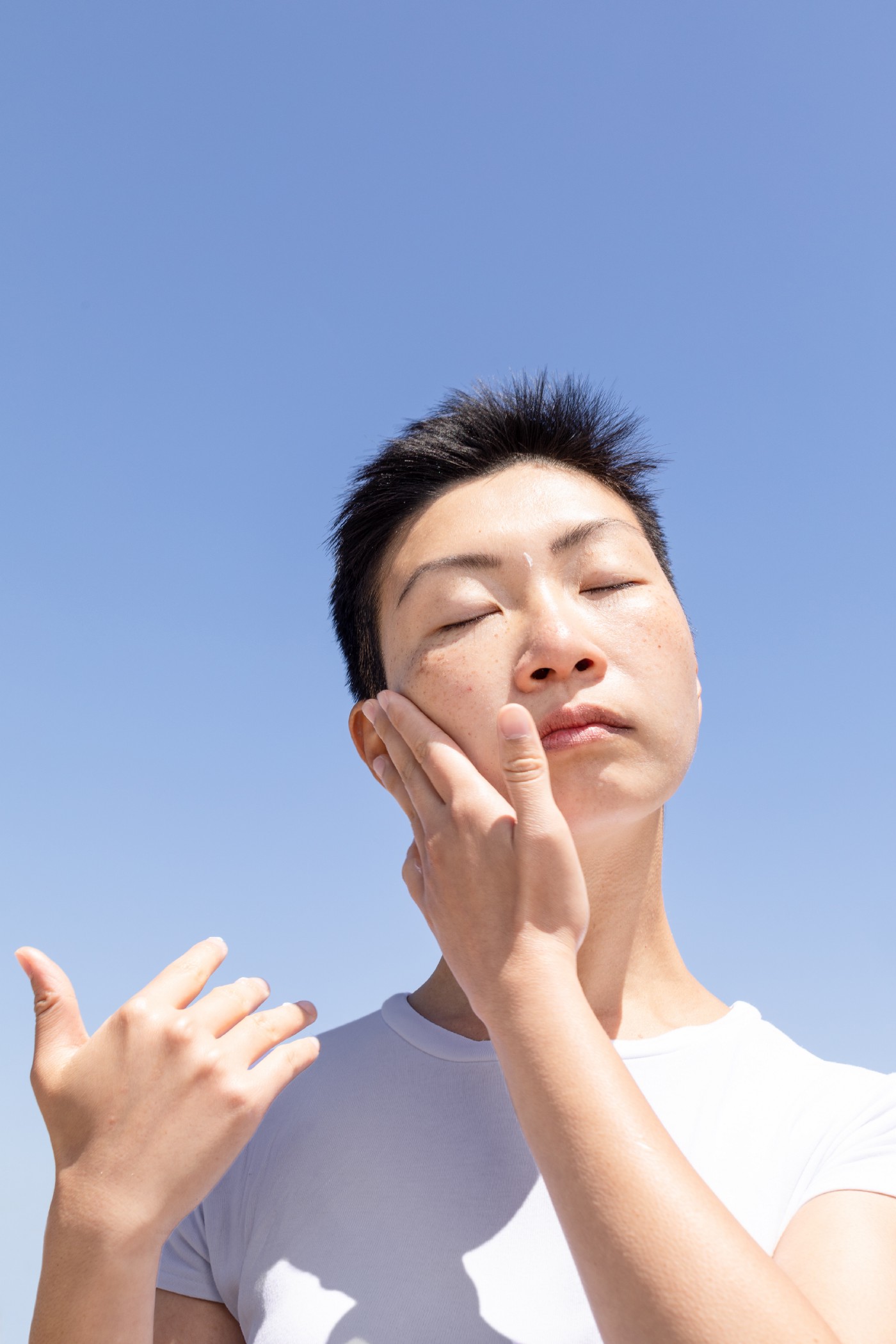 Person in white shirt rubbing skincare cream on face