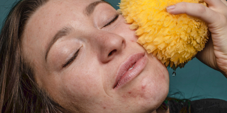 Image of a person with their eyes closed, holding a yellow sponge to their cheek.