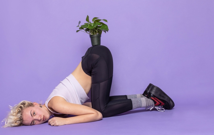 Person holding plant up with their backside | purple background