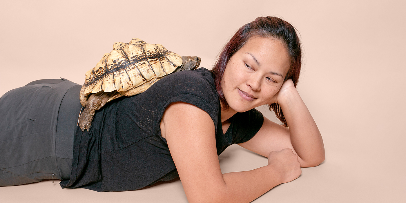 3 A woman laying on her stomach poses with a turtle on her back. 