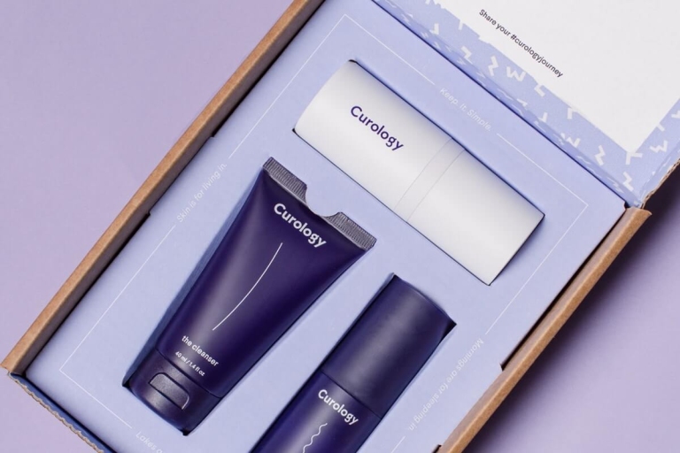 Trial size Curology set, cleanser, moisturizer, and Curology bottle against a purple background
