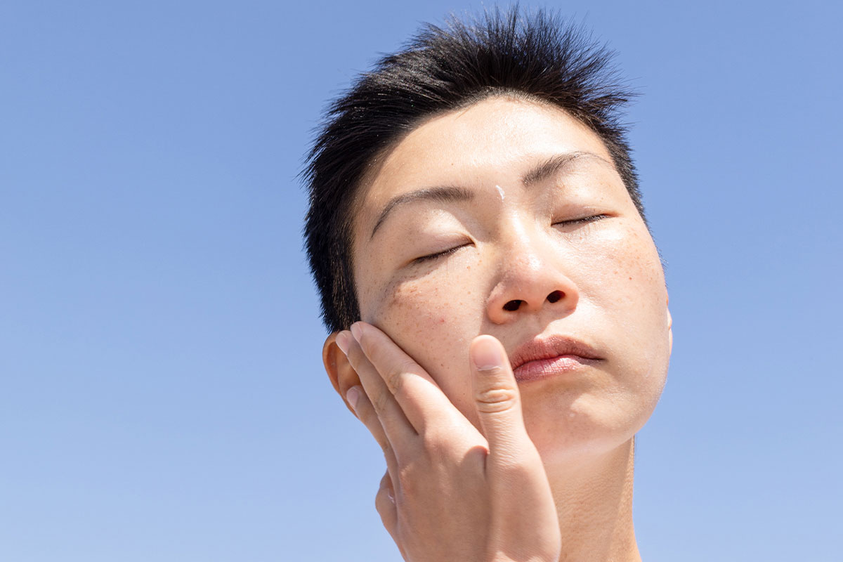 Close-up of a person with their eyes closed, touching the side of their face. 