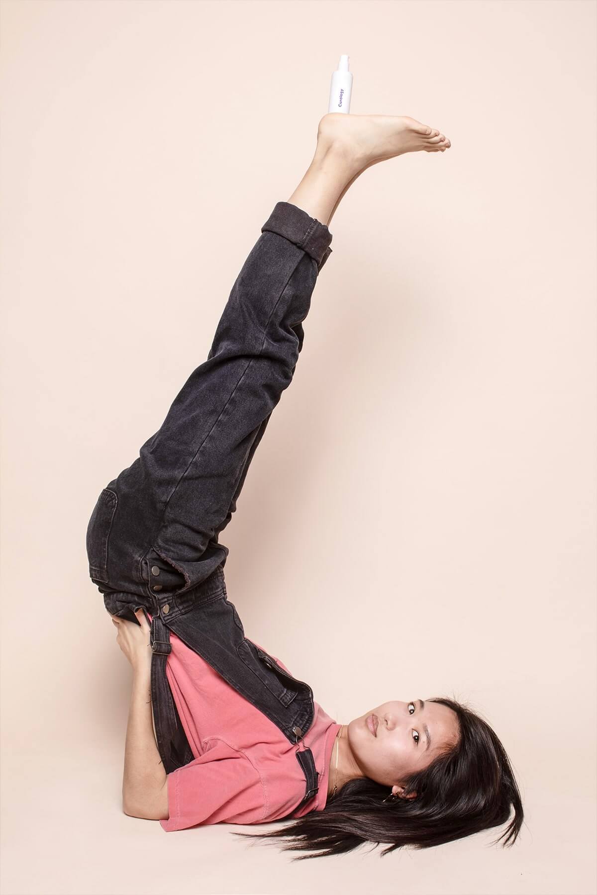 Woman on her back with feet up holding curology bottle 