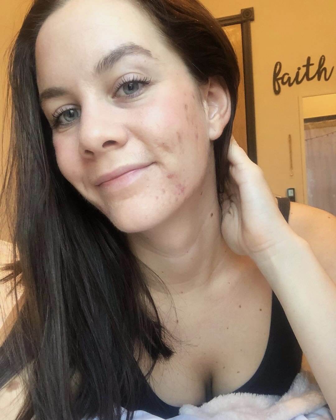 Selfie of woman smiling at camera with "faith" sign in the background (@meghaneblacker , Curology Member)