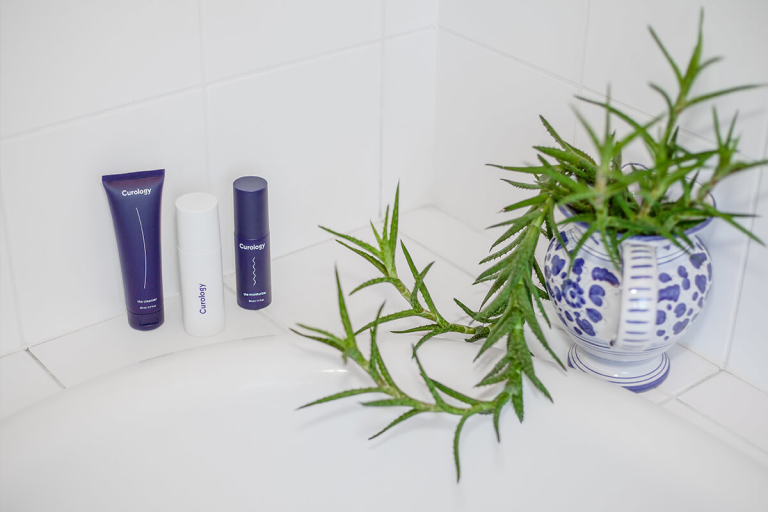 Photograph of a bathtub corner. The Curology set is on the left. An overgrown houseplant is on the right. 