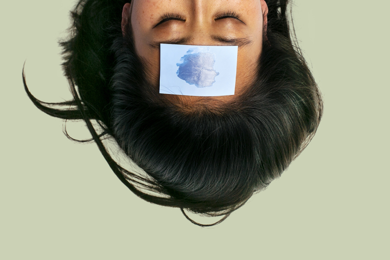 Woman with black hair upside-down with blue blotting paper on forehead against a 