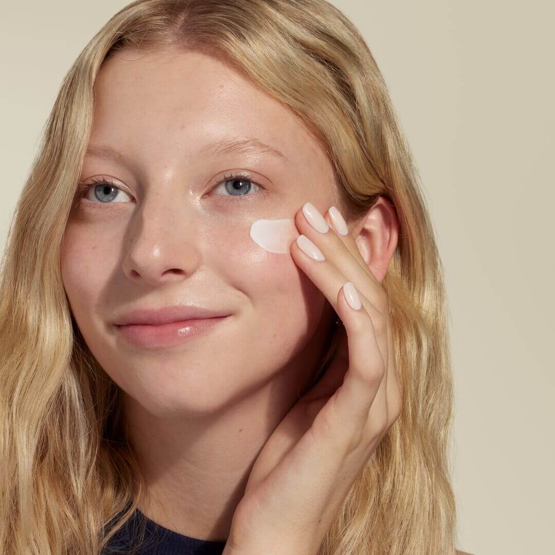 woman putting a white cream on her face