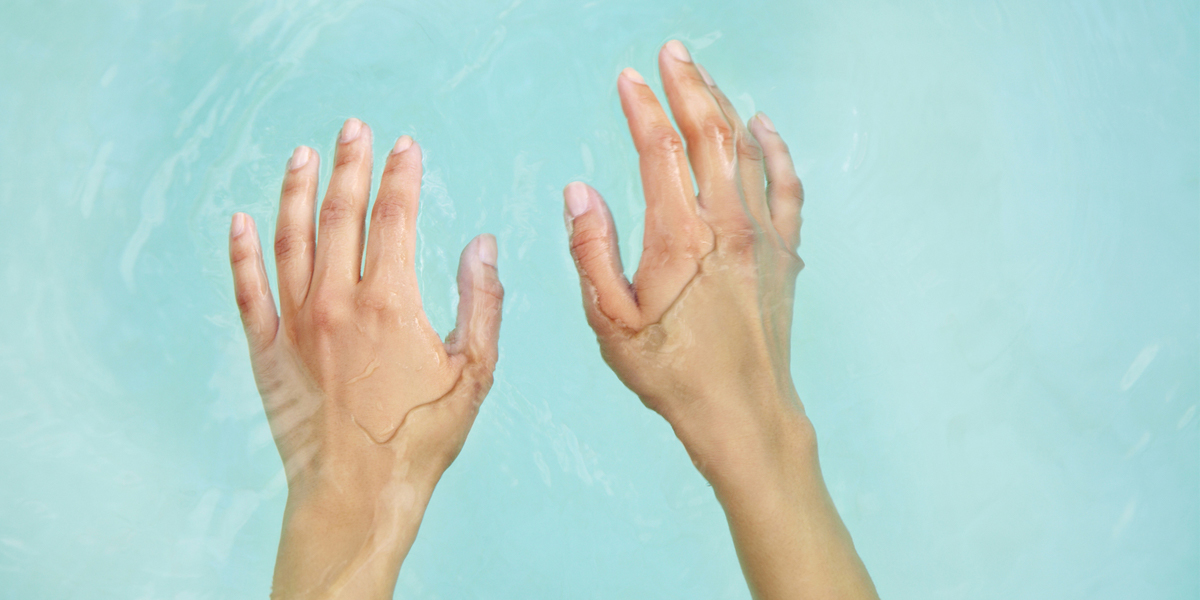 A pair of hands, half-submerged in light blue water. 