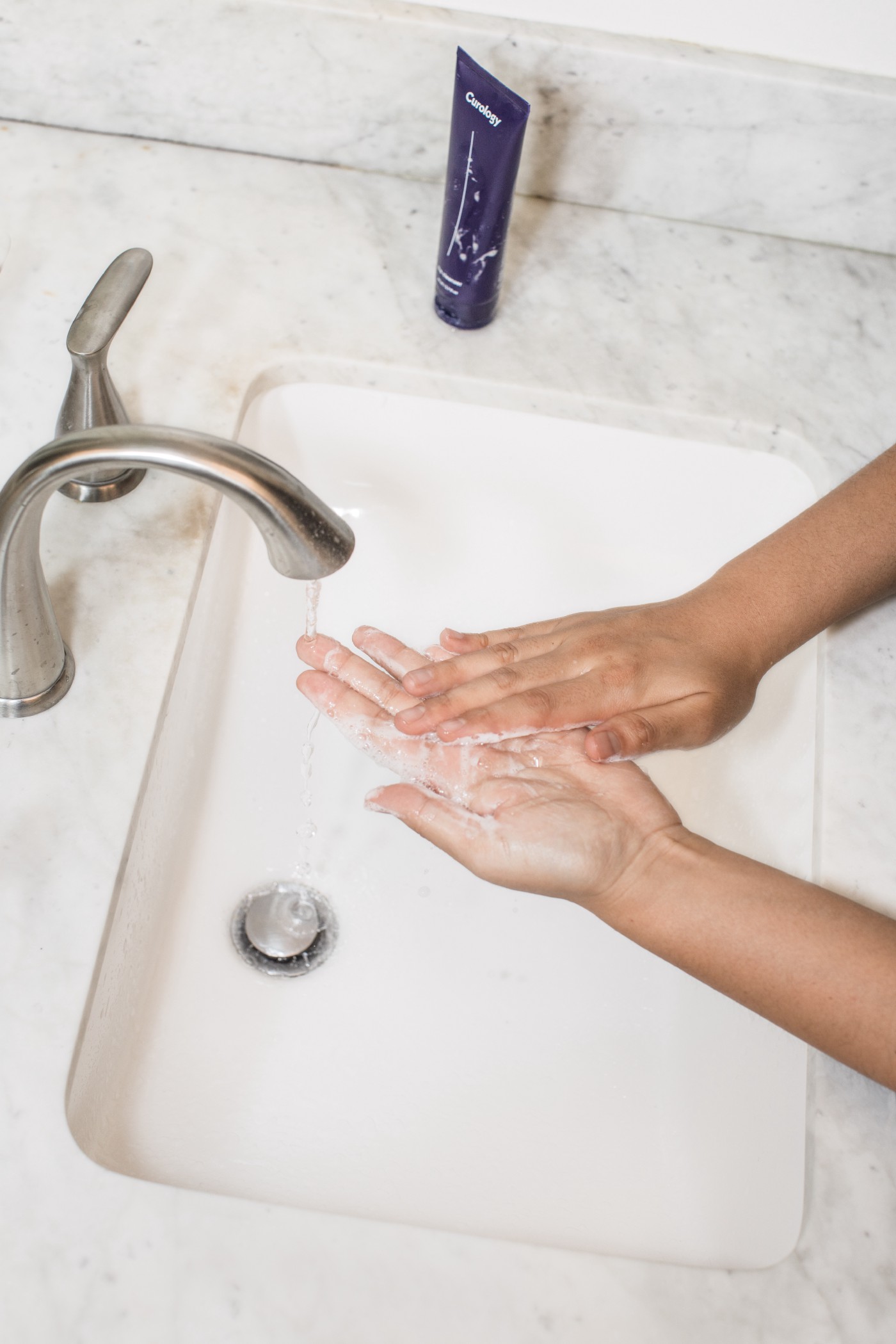 Washing hands in marble sink next to curology bottle