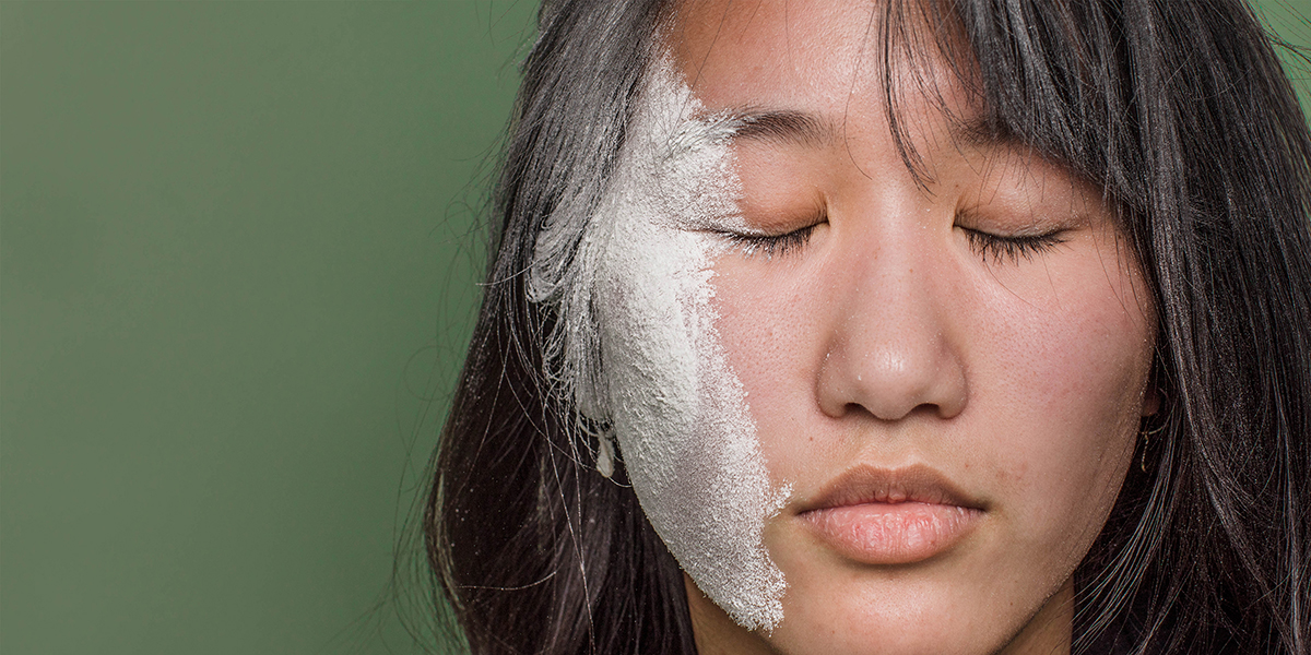 Woman with bangs with pale whitish powder covering cheek, eye, and part of hair against a green background