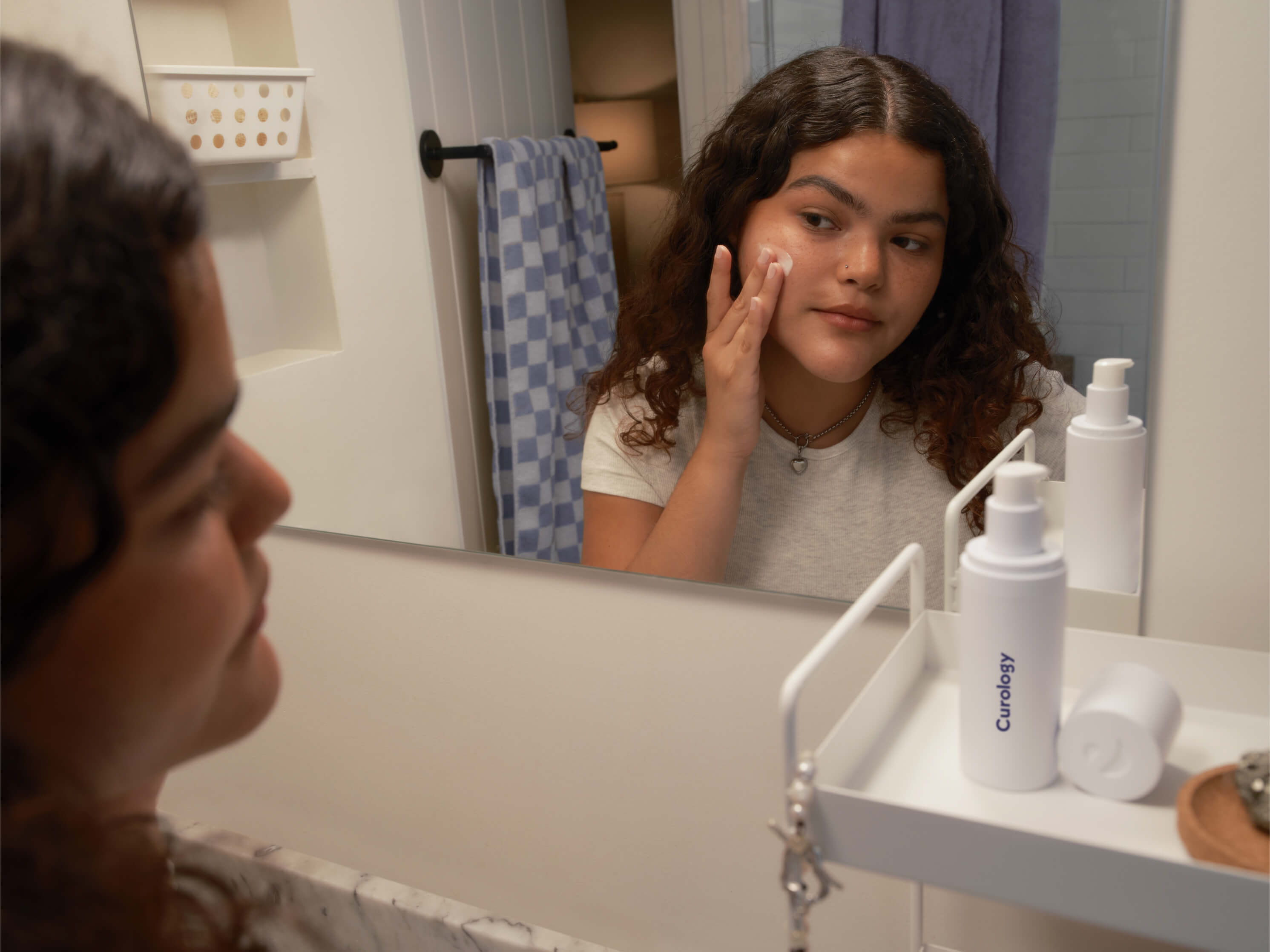 Young brunette with curly hair applying formula in bathroom mirror
