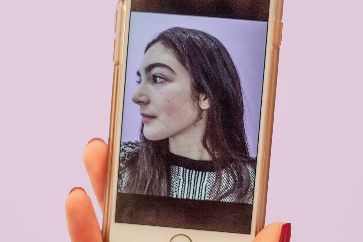 Photograph of a smartphone. On the smartphone's screen is photo of the left side of a woman's face. 