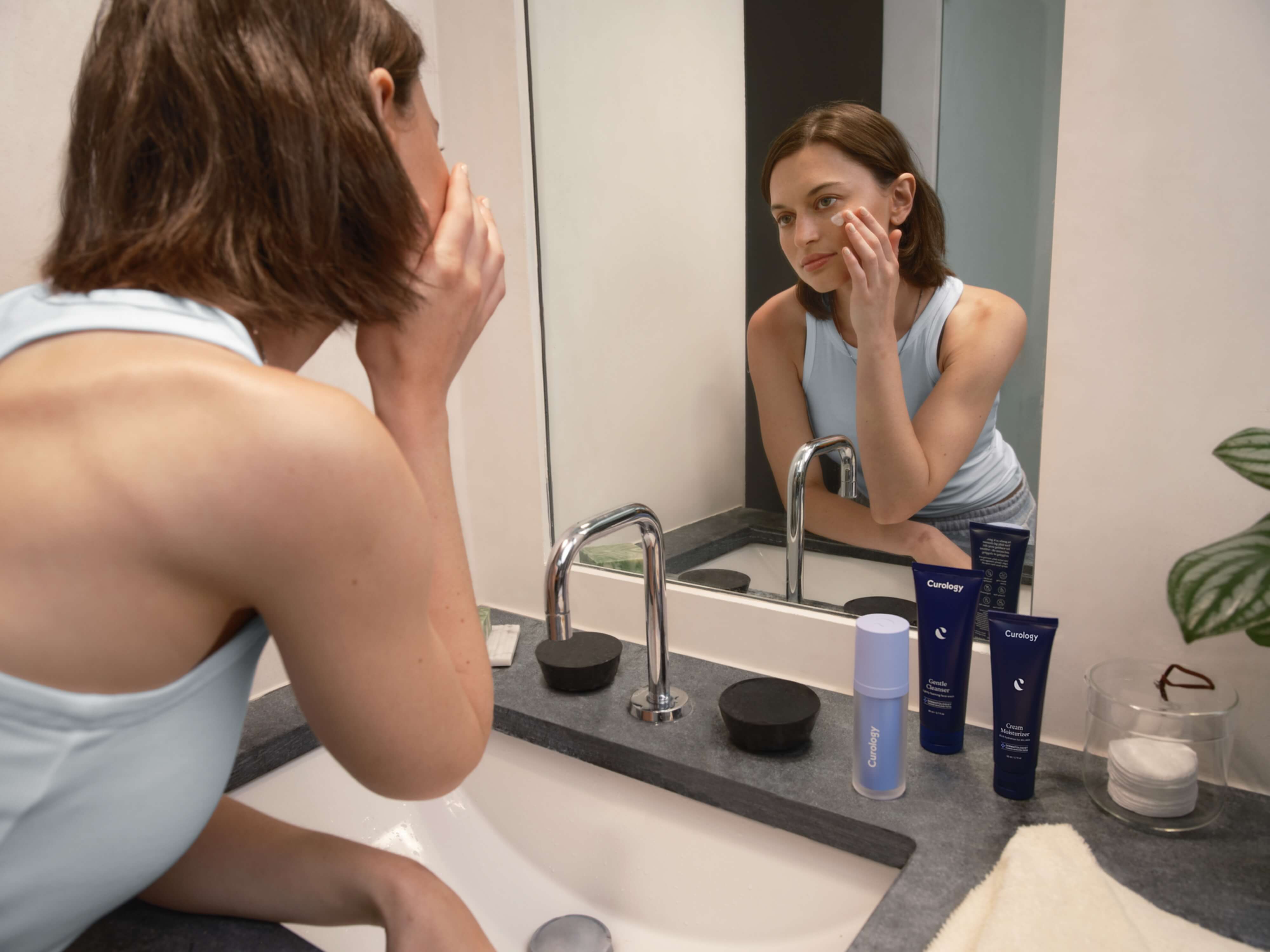 Young brunette with straight hair applying formula in bathroom mirror | Mobile