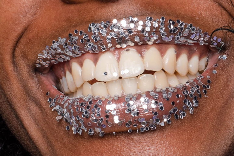 Closeup of smiling mouth with teeth and lips covered in silver glitter