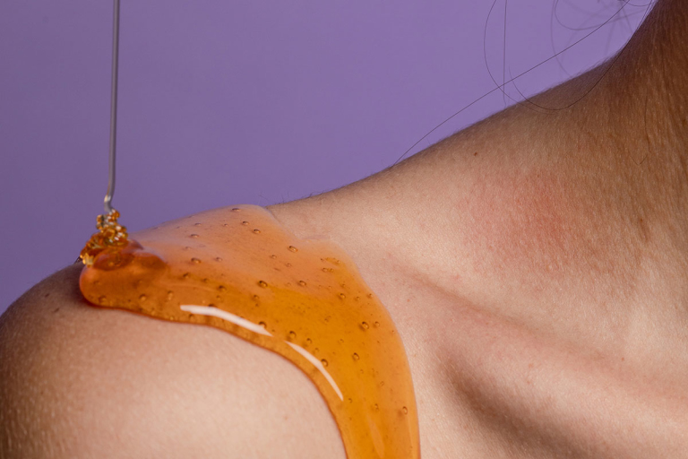 Closeup of a shoulder with golden liquid against a purple background