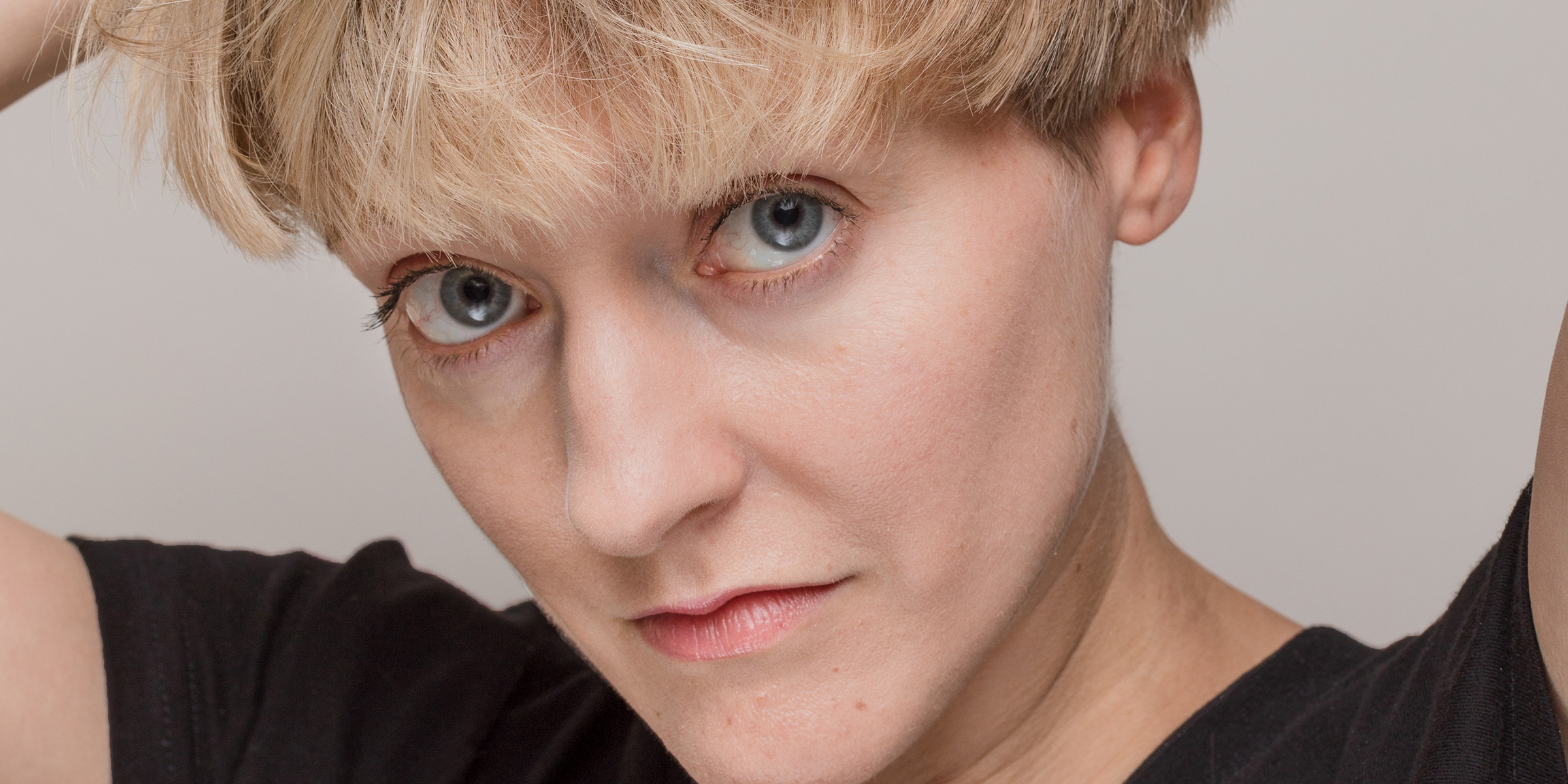 Closeup of a person's face with their hands resting on their head.