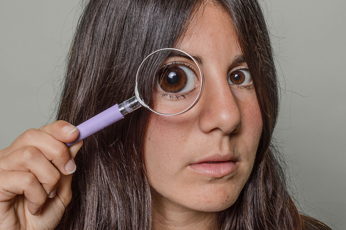 A woman holding a magnifying glass over one of her eyes
