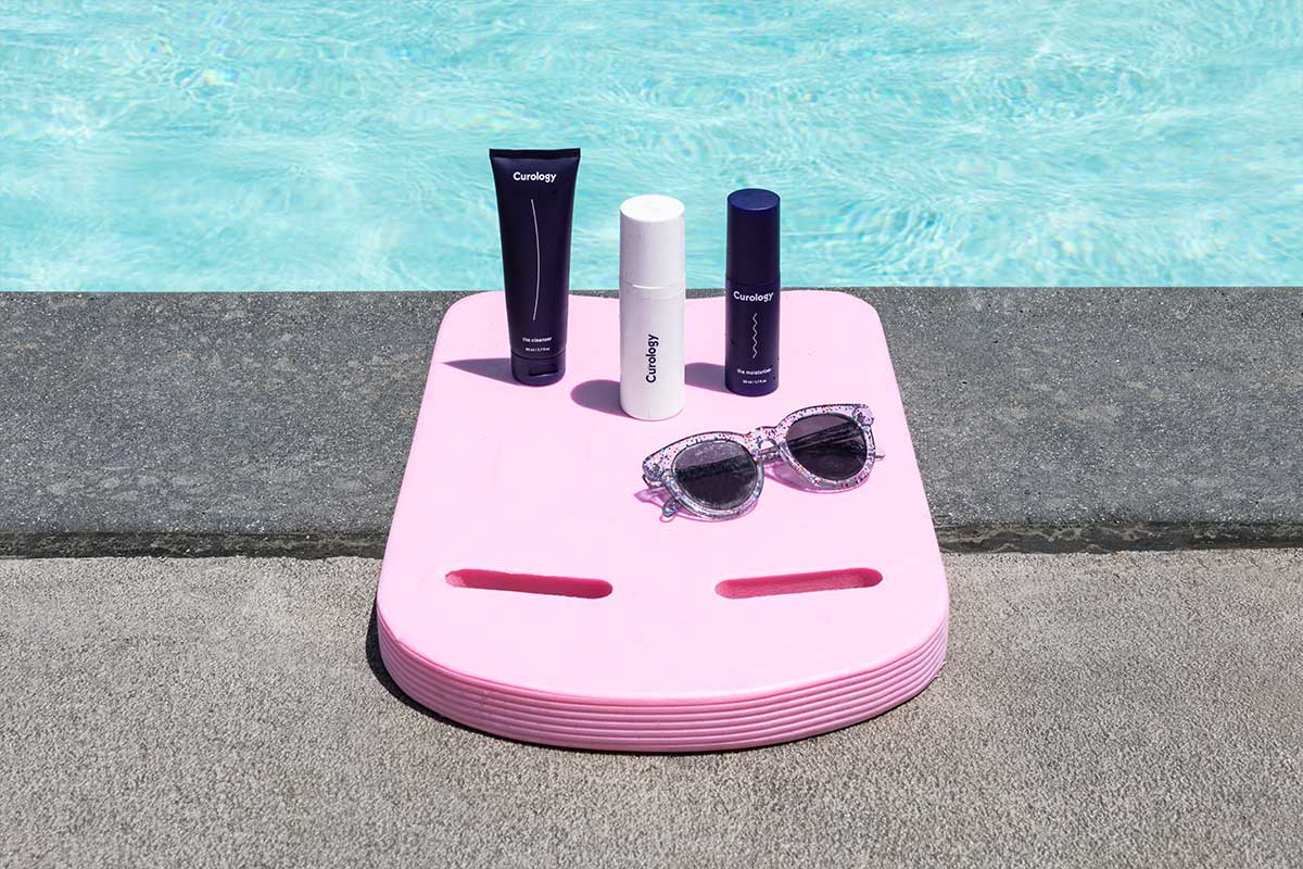 The Curology set sitting on top of a boogie board with sunglasses. A swimming pool is in the background.