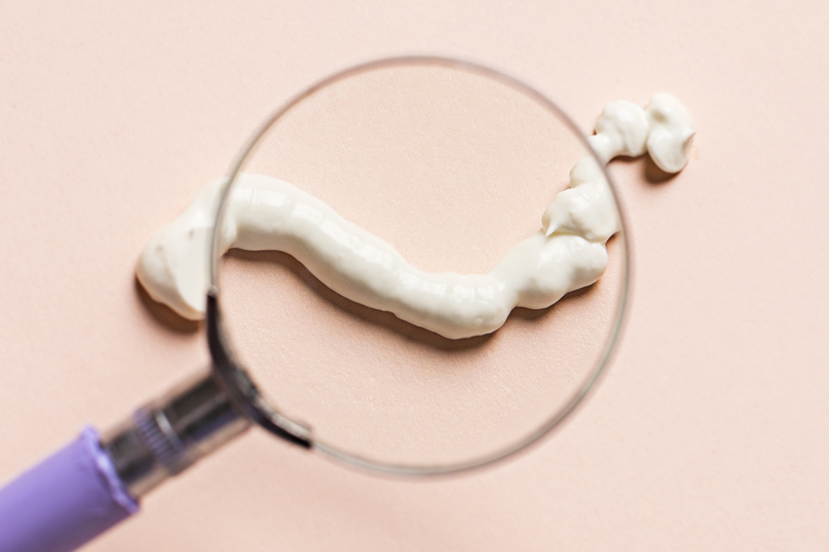 Cream against a peach background with a magnifying glass over it