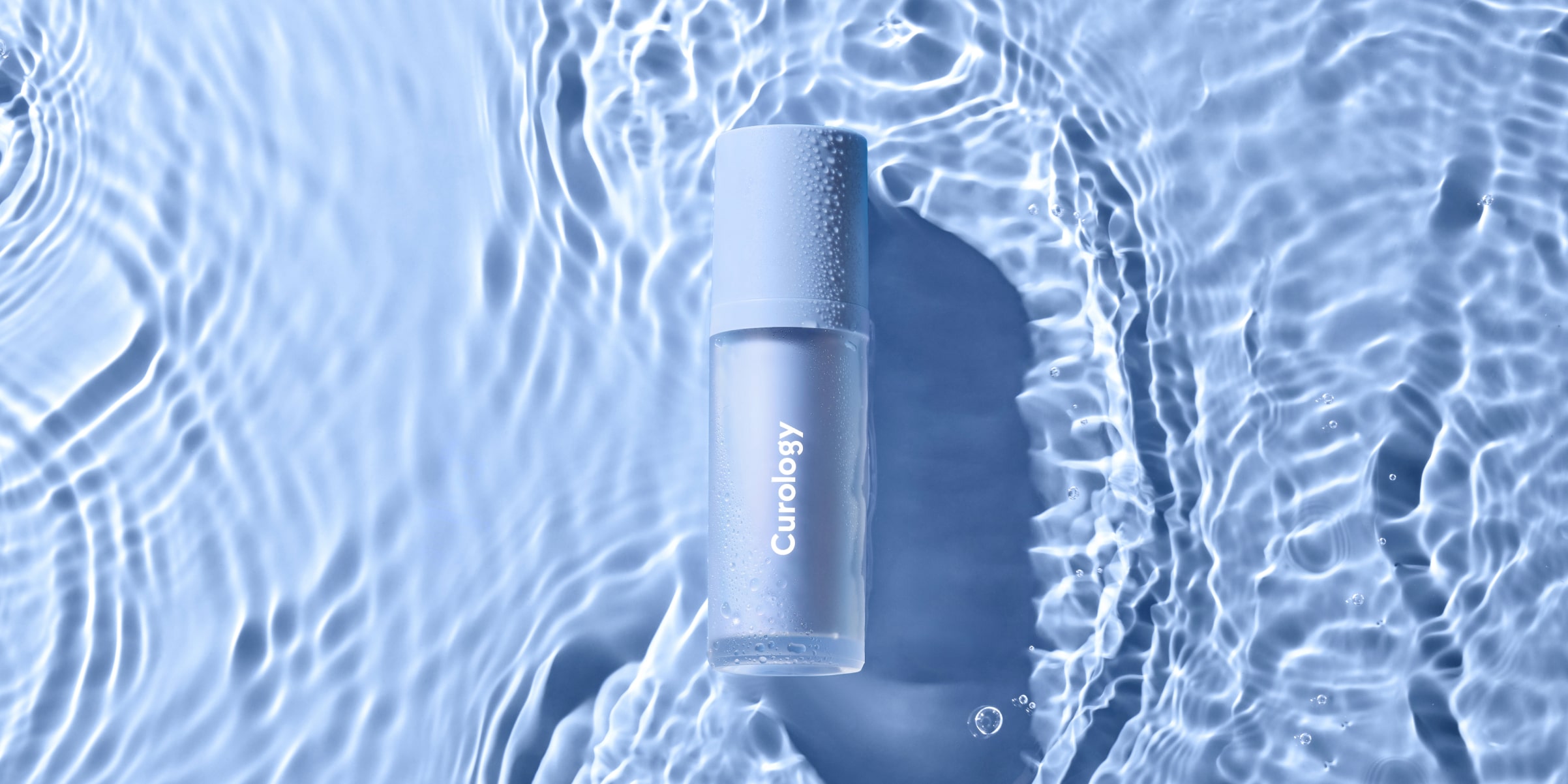 Curology Dayprime Rx treatment and primer bottle with condensation, set against rippling blue water, highlighting prescription skincare designed to hydrate and prep skin for the day