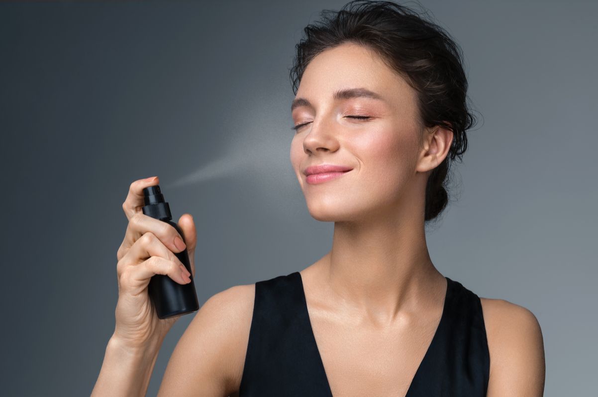 woman applying spray on her makeup face