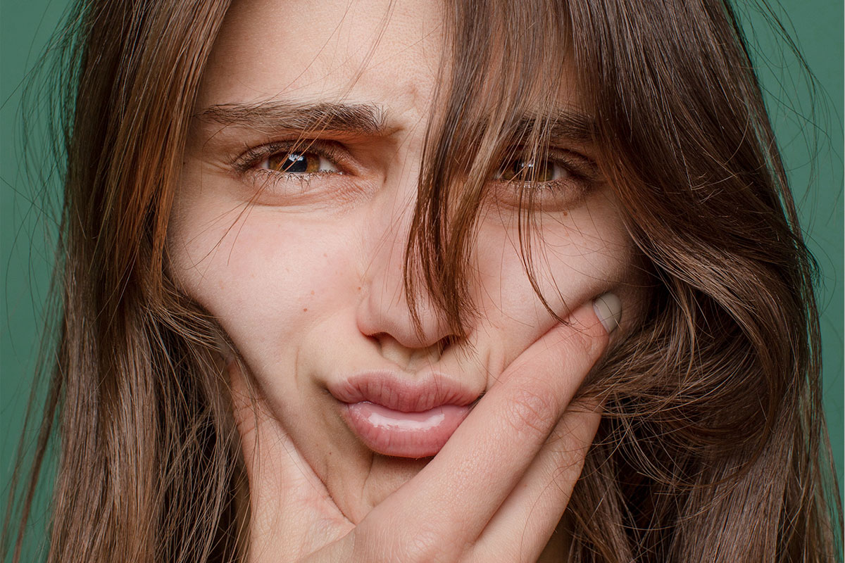 Close-up on a face with a stern expression. They are smooshing their cheeks with one hand.
