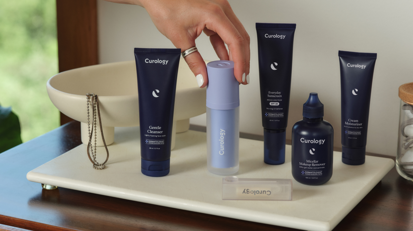 Hand grabbing product on display with other Curology Custom Formula bottles on a white shelf - Desktop