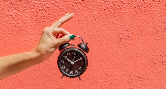 Clock held up by hand against pink background