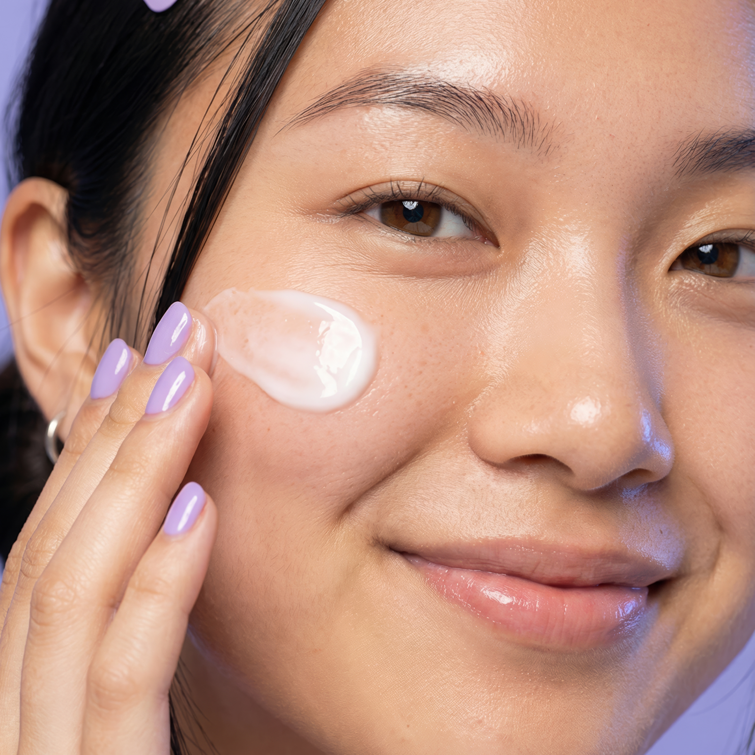 Close-up of a person applying a pea-size amount of skincare cream to their cheek, showing how to apply retinol evenly to the face.