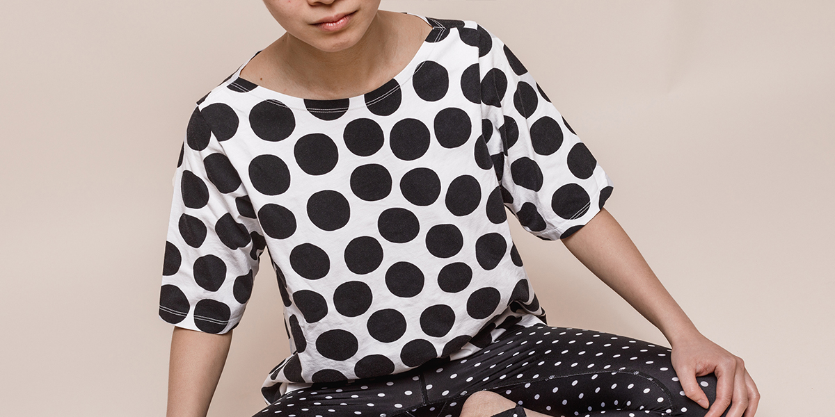 Person wearing white shirt with black dots and black pants with white dots against a neutral background