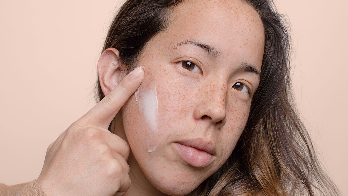 Closeup of woman's face and hand applying cream (large image version)