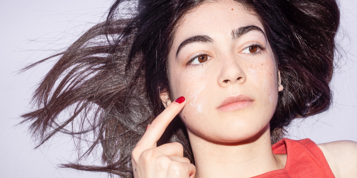 Woman with red fingernail putting skincare cream on face