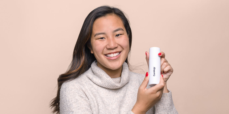 Woman smiling and holding a Curology Custom Formula bottle. 