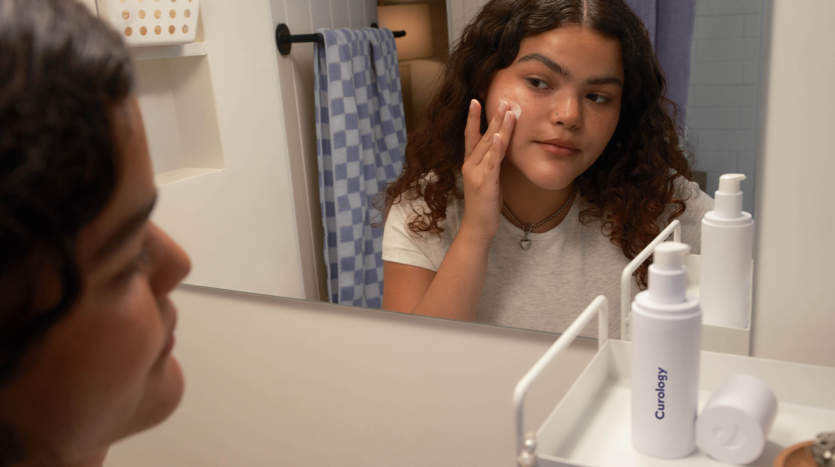 Young brunette with curly hair applying formula in bathroom mirror - Mobile